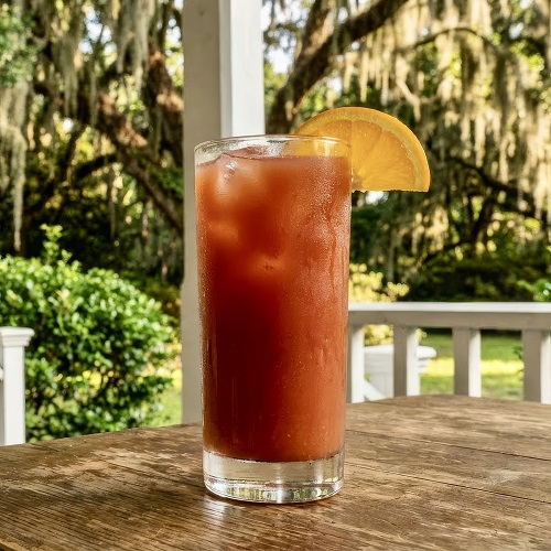 Orange‑red Alabama Slammer cocktail in a Highball glass with ice, garnished with an orange slice.